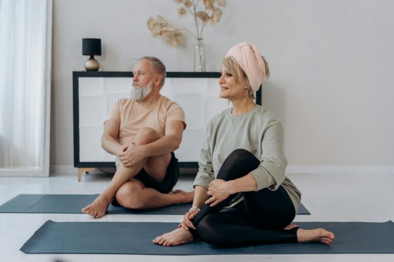 Elderly couple enjoying a relaxing yoga session on mats at home, promoting wellness. (Photo by Mikhail Nilov on Pexels)
