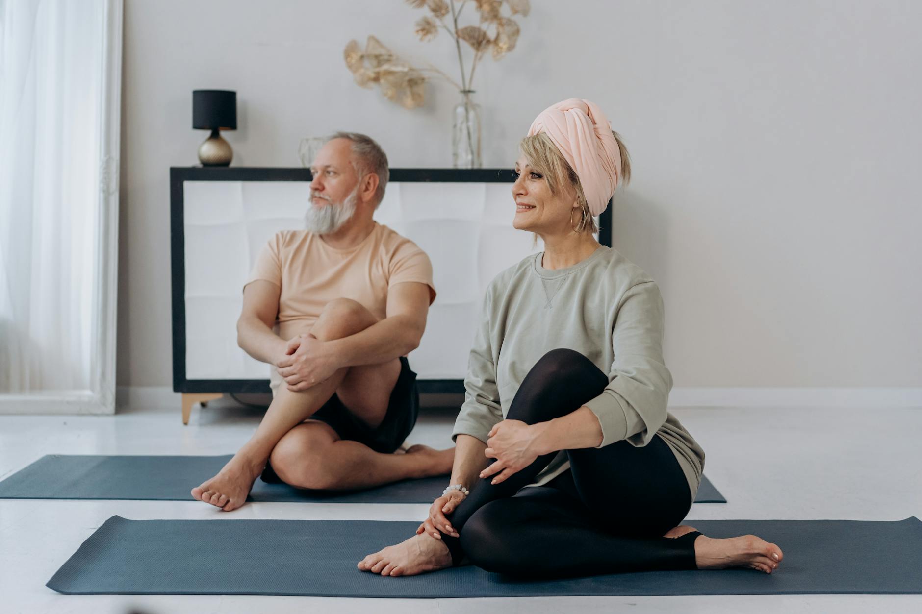 Elderly couple enjoying a relaxing yoga session on mats at home, promoting wellness. (Photo by Mikhail Nilov on Pexels)