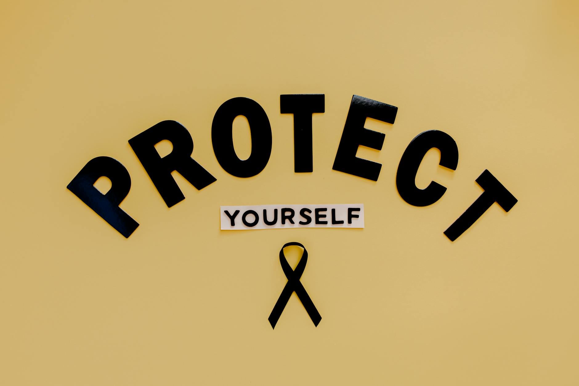 Conceptual awareness image with "Protect Yourself" text and black ribbon on yellow background. (Photo by Tara Winstead on Pexels)