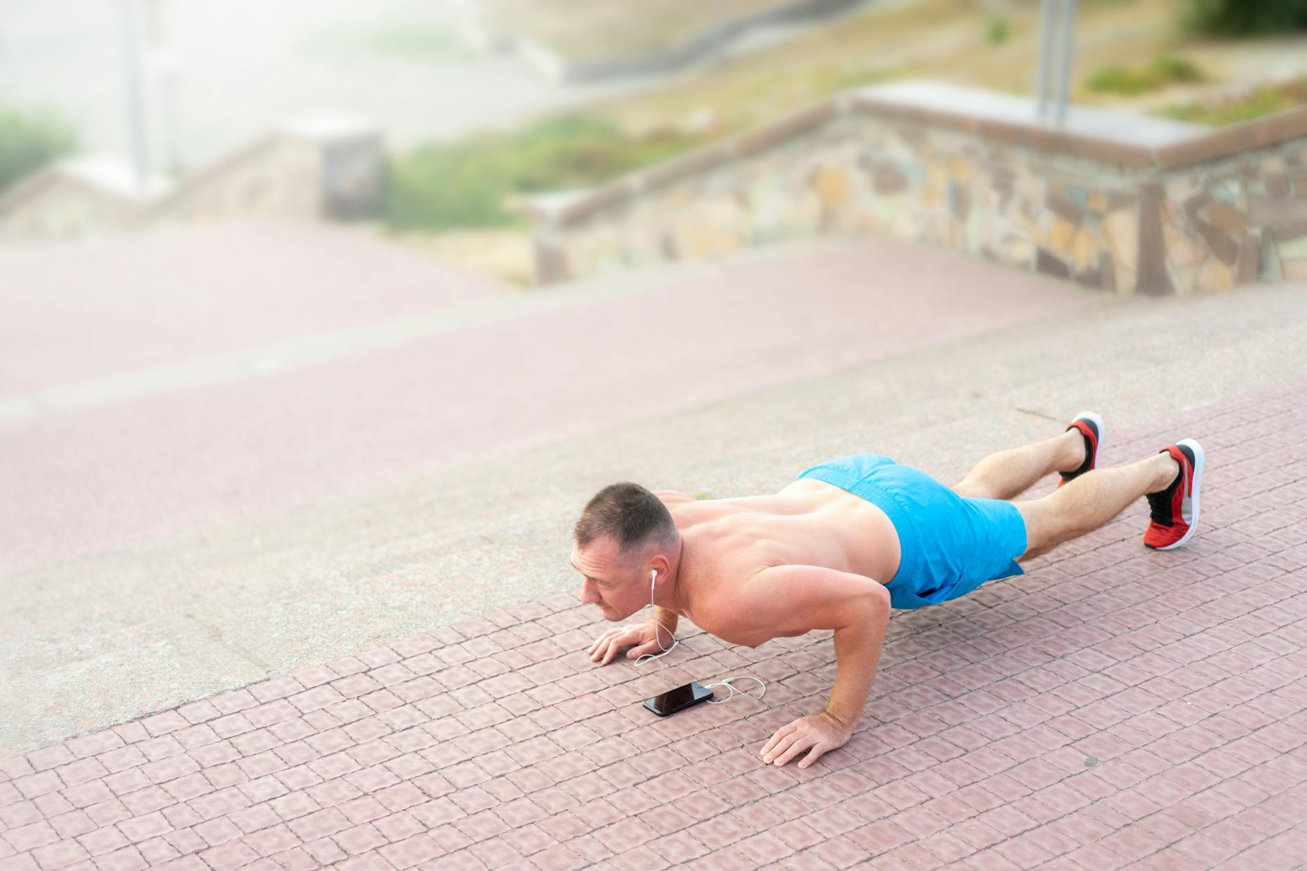 A fit man listening to music and doing push-ups outside on stairs. (Photo by Atlantic Ambience on Pexels)