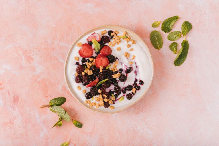 Top view of a vibrant yogurt bowl with mixed berries, granola, and mint leaves on a pink background. (Photo by AI25.Studio  Studio on Pexels)