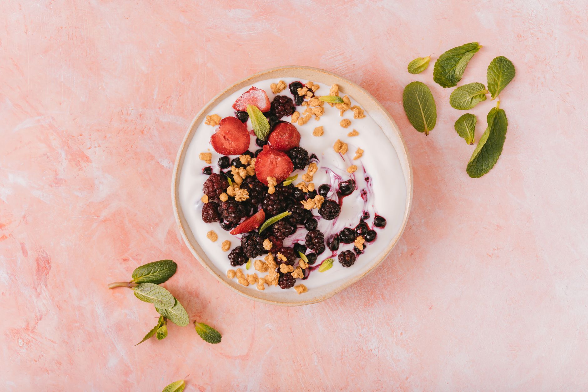 Top view of a vibrant yogurt bowl with mixed berries, granola, and mint leaves on a pink background. (Photo by AI25.Studio  Studio on Pexels)
